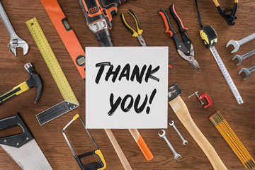 top view of paper with lettering thank you near arranged various tools on wooden table