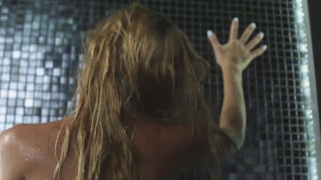 Beautiful sexy blonde girl with wet hair. Posing in a swimsuit in the shower under the drops of water. Slow motion