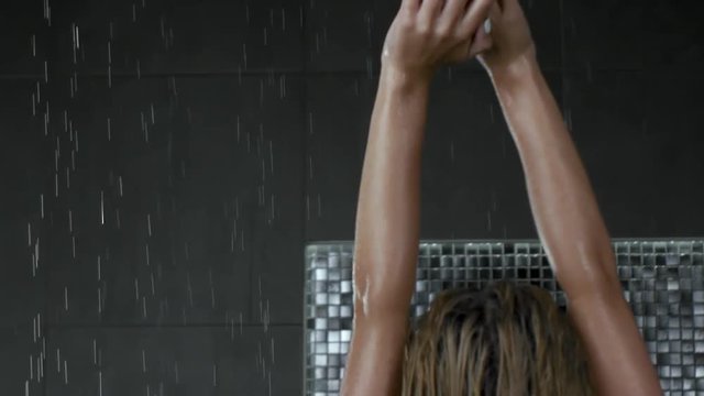 Beautiful sexy blonde girl with wet hair. Posing in a swimsuit in the shower under the drops of water. Slow motion
