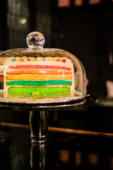 Rainbow layer cake under glass bell dome. Cake stand, dessert storage. Food photography