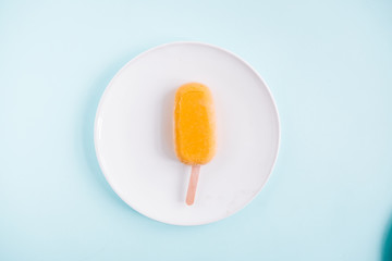 One raw vegan mango popsicle from above. Pastel blue background. Minimalism food photography. Geometric style. Copyspace