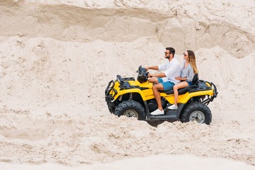 smiling young couple riding all-terrain vehicle in desert
