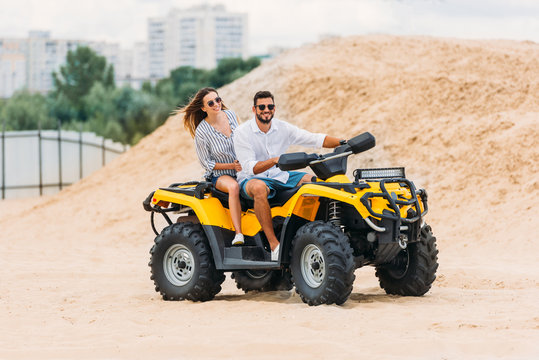 happy active young couple riding all-terrain vehicle in desert