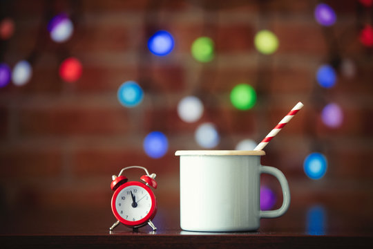 Hot cup of coffee and classic alarm clock with fairy lights on background. Christmas season