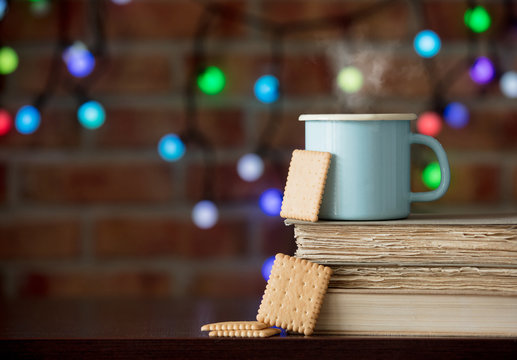 Hot cup of coffee and books with cookie and fairy lights on background. Christmas season
