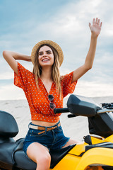 smiling young woman sitting on all-terrain vehicle in desert waving hand © LIGHTFIELD STUDIOS