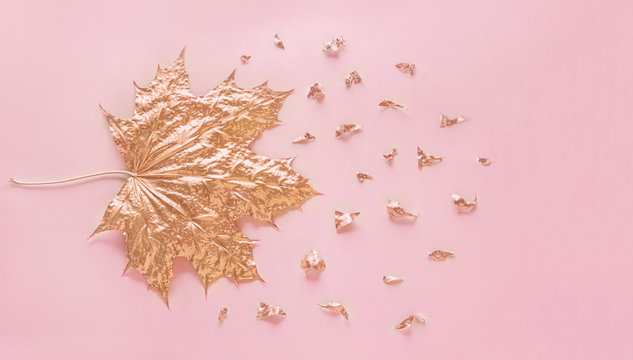 Autumn rose gold maple leaf with elements crumbs on pastel pink paper background. Minimal creative concept with space for text. Top view.
