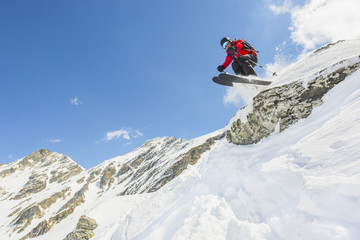 Male skier wearing red jacket jumping in midair off cliff