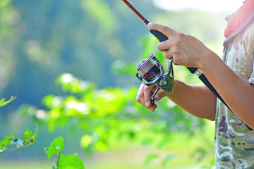 Fishing coil rod in a fisherman hands on a wild river background