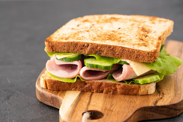 Close-up photo of a club sandwich. Sandwich with meet, prosciutto, salami, salad, vegetables, lettuce on a fresh sliced bread on wooden background. Copy space.