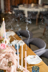 the smoke from the candle. Beautiful and exquisite decoration of the wedding celebration. Banquet served table with a beige pink tablecloth, plates and candlesticks with candles.