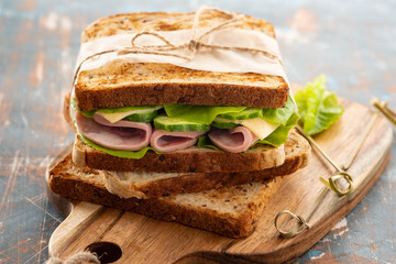 Close-up photo of a club sandwich. Sandwich with meet, prosciutto, salami, salad, vegetables, lettuce on a fresh sliced bread on wooden background. Copy space.