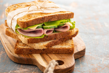 Close-up photo of a club sandwich. Sandwich with meet, prosciutto, salami, salad, vegetables, lettuce on a fresh sliced bread on wooden background. Copy space.