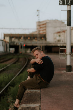 young man sitting in te border of the railway