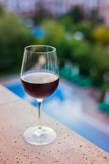 A glass of red wine on the balcony, swimming pool background