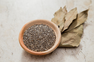 Pottery bowl containing chia seeds. Laurel Nobilis leafs. Marble surface.