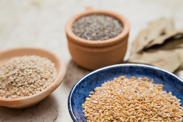 Composition with pottery bowls containing chia seeds, linum seeds, and sesame. Laurel Nobilis leafs. Marble surface.