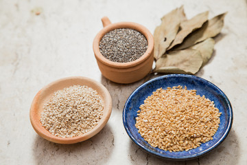 Composition with pottery bowls containing chia seeds, linum seeds, and sesame. Laurel Nobilis leafs. Marble surface.
