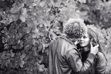 Curly-haired mustachioed man and brown-haired woman hugging in autumn.