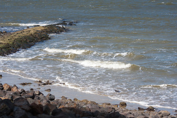 Sea waves crashing against stones lying by the shore. Water and stones on the beach