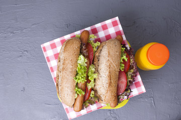 Lunch for school and office in a container and orange juice in a bottle. Sandwich with sausage, salad and cheese. Copy space,