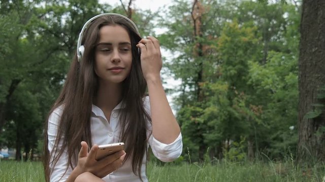 Beautiful girl in headphones on nature. A teenager girl listens to music on headphones in the park.