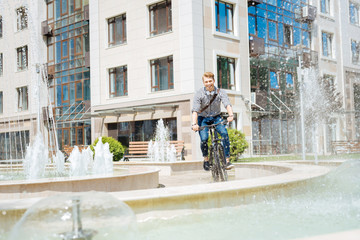 Fototapeta na wymiar Way to work. Positive cheerful man riding near the fountain while going to work