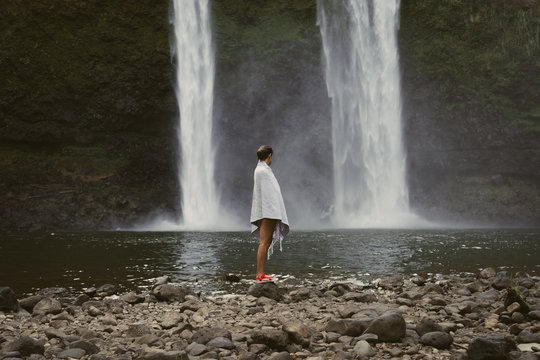 Woman Wrapped in Blanket Standing At The Base Of A Waterfall