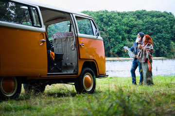 An old hipster couple looks at a road map by their camper van 
