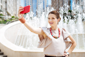 Pleasant memories. Attractive joyful woman smiling while looking into the smartphone camera