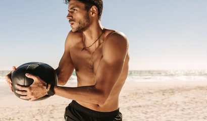 Man training at the beach using a medicine ball