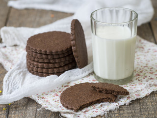 Homemade chocolate cookies with a glass of milk on a wooden background with a lace cloth. Food baking. Copy space, close up