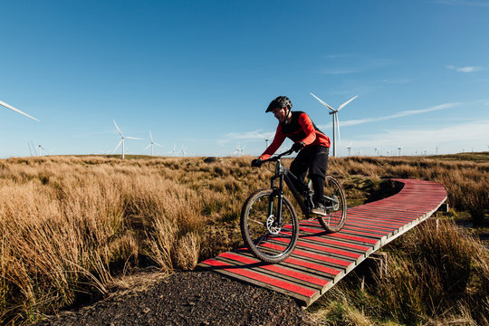 A man in a red and black jersey cycling at speed along a red wooden track at a bike park on a wind farm in Scotland