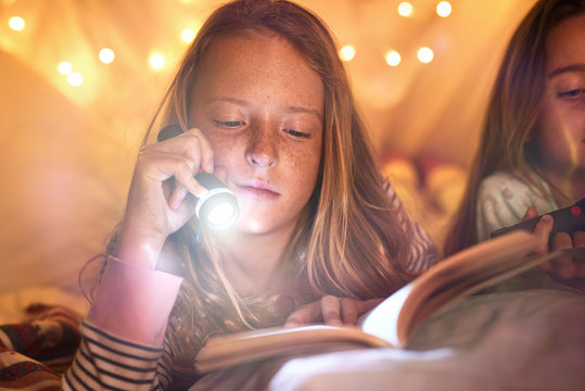 Young girl reading with flashlight in self made fort