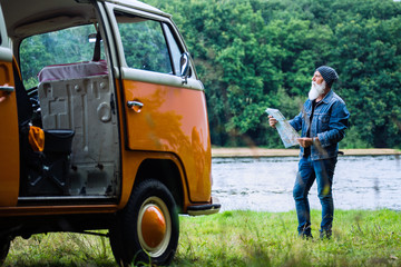 An old hipster man looks at a road map by his camper van 