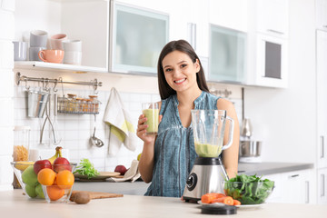 Young woman with tasty healthy smoothie at table in kitchen