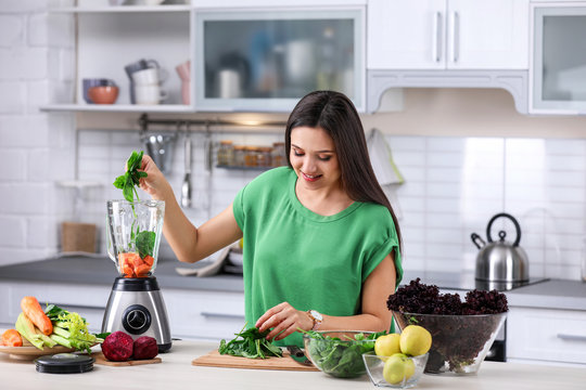 Young woman preparing tasty healthy smoothie at table in kitchen