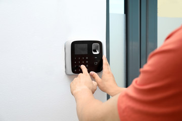 Young man entering code on alarm system keypad indoors