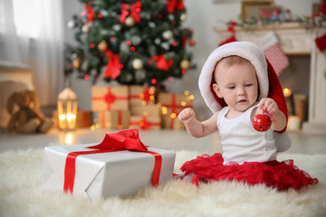 Cute baby in Santa hat playing with jingle bell at home. Christmas celebration