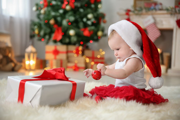 Cute baby in Santa hat playing with jingle bell at home. Christmas celebration