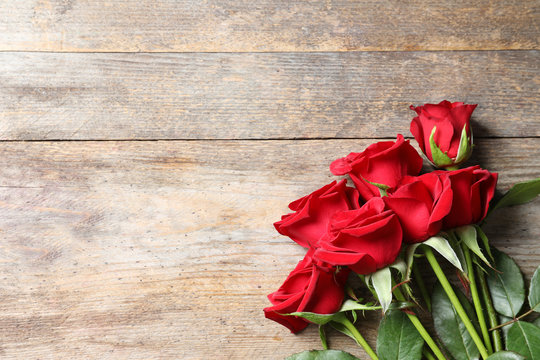 Beautiful red rose flowers on wooden background, top view