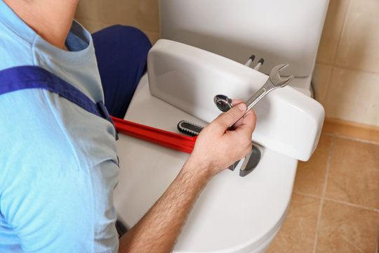 Plumber repairing toilet with wrench indoors, closeup