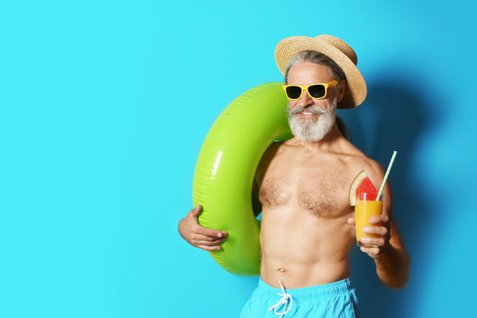 Shirtless man with inflatable ring and glass of cocktail on color background