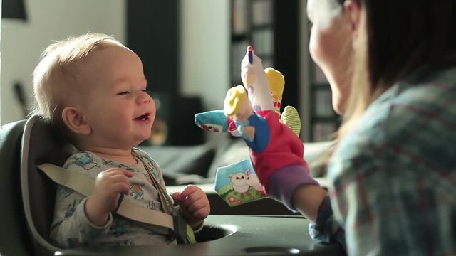 Young mother and her one year old baby son playing with hand puppets at living room
