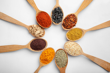 Composition with different aromatic spices in wooden spoons on white background