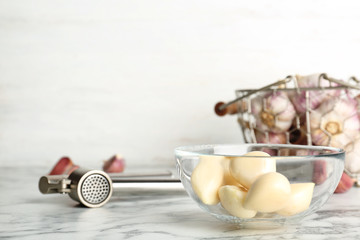 Garlic press and bowl with cloves on marble table