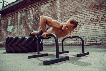 Strong sporty shirtless man doing press exercises holding plank outdoors. Push up from bar. Outdoor training, workout.