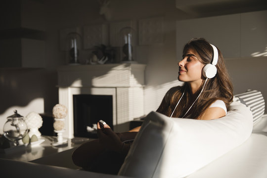 Smiling young woman listening the music on sofa