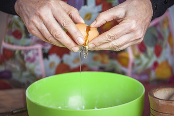Senior old woman's hands breaking an eggshell, letting the yolk and egg white out in the bowl