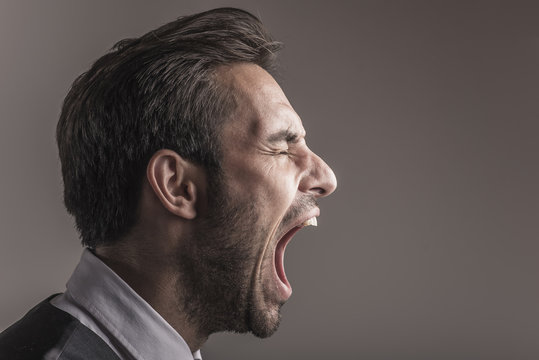 Furious angry young business man shouting and yelling, side view and closeup